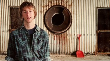Movie still from “Lake Mungo” (2008), directed by Joel Anderson – A man standing in front of a rusted metal wall; Close Up shot, Low angle