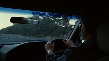 Movie still from “Lake Mungo” (2008), directed by Joel Anderson – A man driving a car on a road; Medium shot, Over the shoulder angle