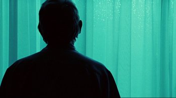 Movie still from “Lake Mungo” (2008), directed by Joel Anderson – A man standing in front of a window with blue curtains; Close Up shot, Low angle
