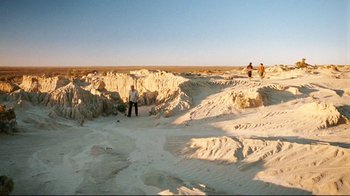 Movie still from “Lake Mungo” (2008), directed by Joel Anderson – Two people standing in the sand on a beach; Extreme Wide shot, High angle