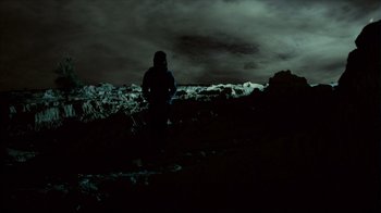 Movie still from “Lake Mungo” (2008), directed by Joel Anderson – A person standing on top of a hill under a cloudy sky; Extreme Wide shot, Low angle