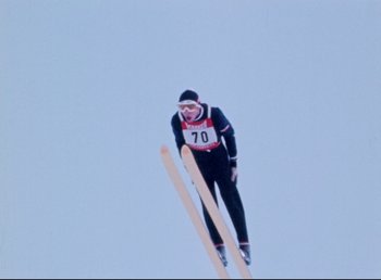 Movie still from “Land of Silence and Darkness” (1971), directed by Werner Herzog – A man flying through the air while riding skis; Wide shot, Low angle