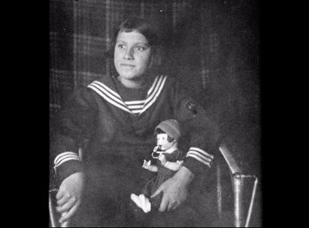 Movie still from “Land of Silence and Darkness” (1971), directed by Werner Herzog – An old black and white photo of a girl holding a doll; Medium shot, High angle