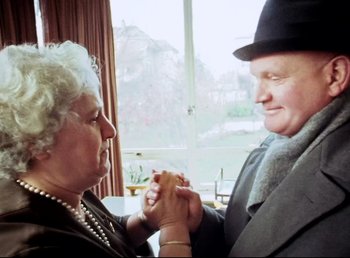Movie still from “Land of Silence and Darkness” (1971), directed by Werner Herzog – An older couple holding hands in front of a window; Close Up shot, Over the shoulder angle