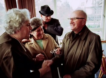 Movie still from “Land of Silence and Darkness” (1971), directed by Werner Herzog – A group of people standing next to each other in a room; Medium shot, Over the shoulder angle