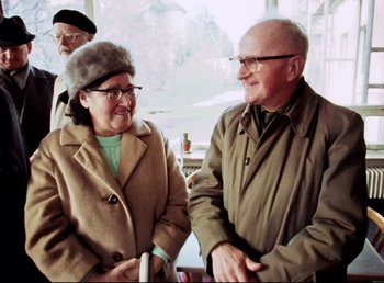Movie still from “Land of Silence and Darkness” (1971), directed by Werner Herzog – An older man and woman are smiling for the camera; Medium shot, High angle