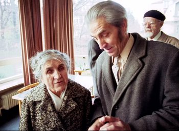 Movie still from “Land of Silence and Darkness” (1971), directed by Werner Herzog – An older man standing next to an older woman; Medium shot, Over the shoulder angle