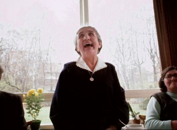 Movie still from “Land of Silence and Darkness” (1971), directed by Werner Herzog – An older woman is laughing in front of a window; Medium shot, Over the shoulder angle