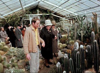 Movie still from “Land of Silence and Darkness” (1971), directed by Werner Herzog – A group of people standing around a cactus garden; Wide shot, Over the shoulder angle
