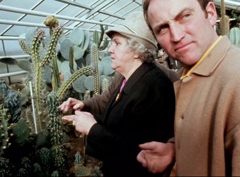 Movie still from “Land of Silence and Darkness” (1971), directed by Werner Herzog – Two people standing next to each other in a greenhouse; Medium shot, Low angle