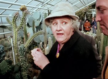 Movie still from “Land of Silence and Darkness” (1971), directed by Werner Herzog – An older woman wearing a hat and holding a plant; Close Up shot, High angle