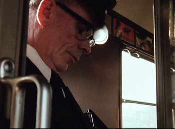 Movie still from “Land of Silence and Darkness” (1971), directed by Werner Herzog – A man wearing a hat and glasses on a bus; Close Up shot, Low angle