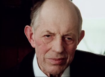 Movie still from “Land of Silence and Darkness” (1971), directed by Werner Herzog – An older man in a black suit and white shirt; Close Up shot, Low angle