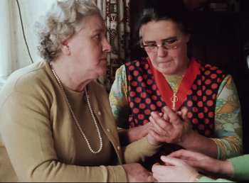 Movie still from “Land of Silence and Darkness” (1971), directed by Werner Herzog – Two older women sitting in front of each other holding hands; Medium shot, High angle