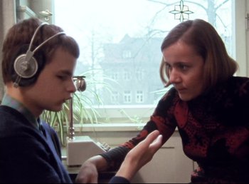 Movie still from “Land of Silence and Darkness” (1971), directed by Werner Herzog – A woman and a young boy wearing headphones; Medium shot, Over the shoulder angle
