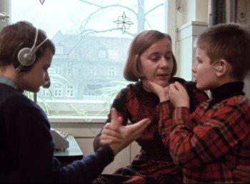Movie still from “Land of Silence and Darkness” (1971), directed by Werner Herzog – A woman and two boys are talking to each other; Medium shot, Over the shoulder angle