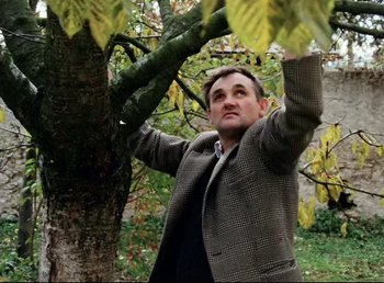 Movie still from “Land of Silence and Darkness” (1971), directed by Werner Herzog – A man standing next to a tree in a park; Medium shot, Low angle