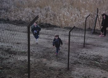 Movie still from “Landscape in the Mist” (1988), directed by Theodoros Angelopoulos – Two children running through a fence on a dirt road; Extreme Wide shot, High angle