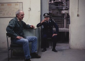 Movie still from “Landscape in the Mist” (1988), directed by Theodoros Angelopoulos – A man sitting next to another man on a bench; Wide shot, High angle