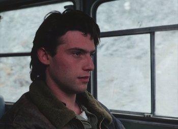 Movie still from “Landscape in the Mist” (1988), directed by Theodoros Angelopoulos – A young man with long dark hair is sitting on a bus; Close Up shot, Over the shoulder angle