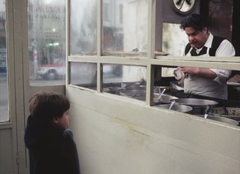 Movie still from “Landscape in the Mist” (1988), directed by Theodoros Angelopoulos – A man in an apron cooking food in a kitchen; Medium shot, Over the shoulder angle