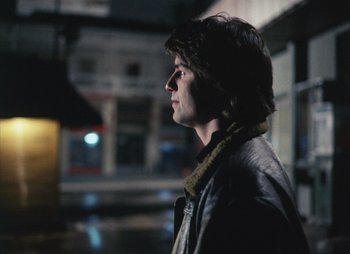 Movie still from “Landscape in the Mist” (1988), directed by Theodoros Angelopoulos – A man in a leather jacket looking to his left; Medium shot, Over the shoulder angle