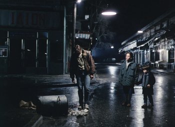 Movie still from “Landscape in the Mist” (1988), directed by Theodoros Angelopoulos – A group of people walking down a street at night; Wide shot, High angle