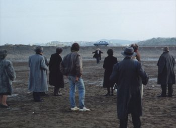 Movie still from “Landscape in the Mist” (1988), directed by Theodoros Angelopoulos – A group of people standing on top of a sandy beach; Extreme Wide shot, High angle