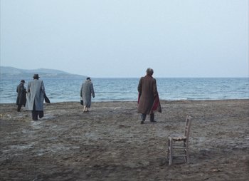 Movie still from “Landscape in the Mist” (1988), directed by Theodoros Angelopoulos – A group of people standing on top of a sandy beach next to the ocean; Extreme Wide shot, High angle