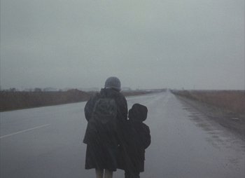 Movie still from “Landscape in the Mist” (1988), directed by Theodoros Angelopoulos – A woman and a child walking down a road; Wide shot, Low angle