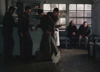 Movie still from “Landscape in the Mist” (1988), directed by Theodoros Angelopoulos – A group of men standing around a kitchen with a turkey; Wide shot, High angle