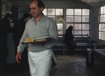 Movie still from “Landscape in the Mist” (1988), directed by Theodoros Angelopoulos – A man carrying a tray of food while walking in a train station; Medium shot, Over the shoulder angle