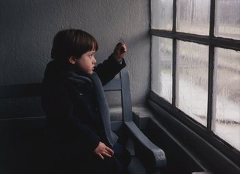 Movie still from “Landscape in the Mist” (1988), directed by Theodoros Angelopoulos – A young boy sitting in front of a window; Medium shot, Low angle