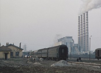 Movie still from “Landscape in the Mist” (1988), directed by Theodoros Angelopoulos – A train traveling down train tracks next to a building; Extreme Wide shot, Low angle