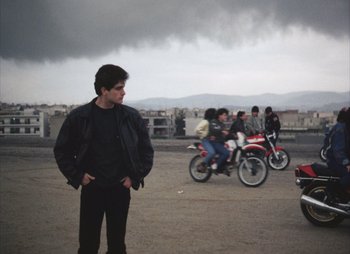 Movie still from “Landscape in the Mist” (1988), directed by Theodoros Angelopoulos – A man standing in a parking lot next to motorcycles; Wide shot, Low angle