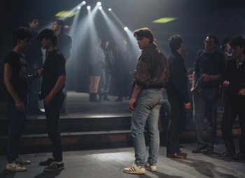 Movie still from “Landscape in the Mist” (1988), directed by Theodoros Angelopoulos – A group of people standing on a stage with spotlights in the background; Wide shot, Over the shoulder angle