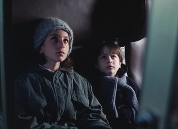 Movie still from “Landscape in the Mist” (1988), directed by Theodoros Angelopoulos – Two young children sitting on a train looking at the camera; Close Up shot, High angle