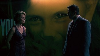 Movie still from “Lantana” (2001), directed by Ray Lawrence – A man and a woman standing in front of a wall with a picture of a woman's face on it; Medium shot, Low angle