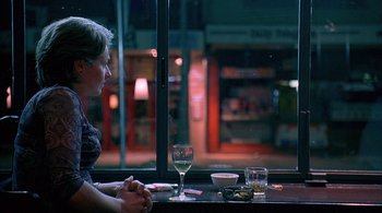 Movie still from “Lantana” (2001), directed by Ray Lawrence – A woman sitting at a table with a glass of wine; Medium shot, Over the shoulder angle