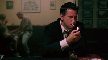 Movie still from “Lantana” (2001), directed by Ray Lawrence – A man in a suit lighting a cigarette in a bar; Medium shot, Low angle