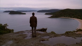 A man standing on top of a hill looking at the water