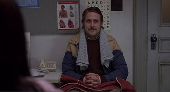 Movie still from “Lars and the Real Girl” (2007), directed by Craig Gillespie – A man sitting at a desk in front of an eye chart; Medium shot, Over the shoulder angle