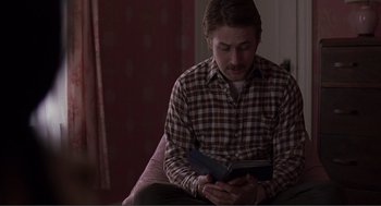Movie still from “Lars and the Real Girl” (2007), directed by Craig Gillespie – A man sitting on a couch reading a book; Medium shot, Over the shoulder angle