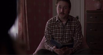 Movie still from “Lars and the Real Girl” (2007), directed by Craig Gillespie – A man sitting on a couch holding a book; Medium shot, Over the shoulder angle
