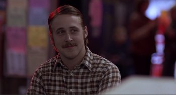 Movie still from “Lars and the Real Girl” (2007), directed by Craig Gillespie – A man with long hair and a mustache is smiling for the camera; Close Up shot, Over the shoulder angle