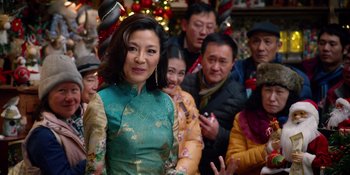 Movie still from “Last Christmas” (2019), directed by Paul Feig – A group of people gathered around a woman in a green dress; Medium shot, Over the shoulder angle