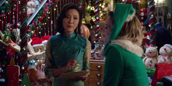 Movie still from “Last Christmas” (2019), directed by Paul Feig – Two women dressed up in green and one of them is holding a clipboard; Medium shot, Over the shoulder angle