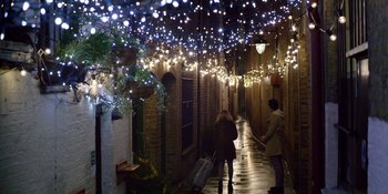 Movie still from “Last Christmas” (2019), directed by Paul Feig – Two people walking down a street under a string of lights at night; Extreme Wide shot, Over the shoulder angle