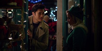 Movie still from “Last Christmas” (2019), directed by Paul Feig – A man and a woman standing next to each other in front of christmas lights; Medium shot, Over the shoulder angle