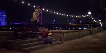 Movie still from “Last Christmas” (2019), directed by Paul Feig – A woman sitting on steps next to a man on a bridge; Wide shot, High angle